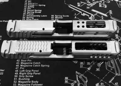 Two custom-machined gun slides on a parts diagram mat.